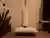 Joovv red light therapy panel mounted vertically on a stand in a townhouse corner, with a white floor pillow and rolled yoga mat below it for seiza meditation, a snake plant to the left and a coat rack to the right